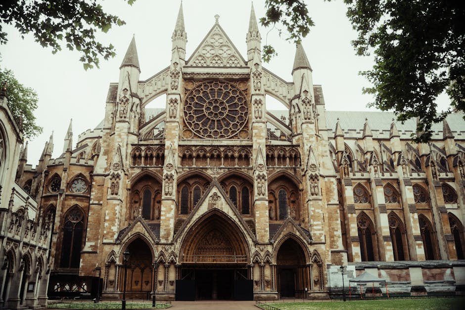 A detailed floral arrangement featuring a bouquet of fresh flowers held in a person's hands, positioned in front of Westminster Abbey. The bouquet includes large, vibrant roses in shades of pink and r