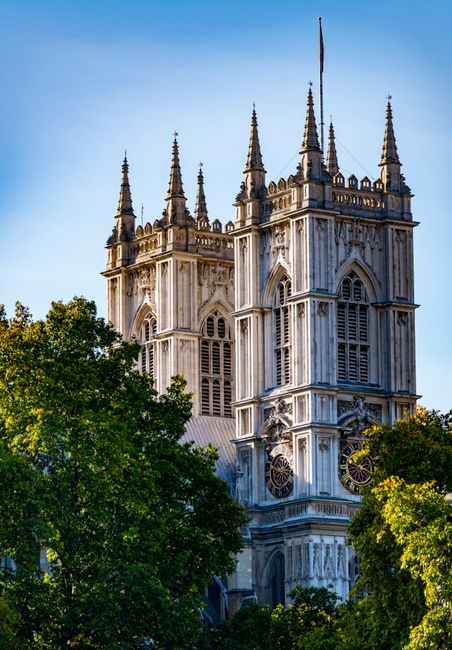 A close-up view of Westminster Abbey's twin towers, featuring detailed Gothic architectural elements, with weathered stone surfaces and intricate tracery. The towers are adorned with tall spires and d