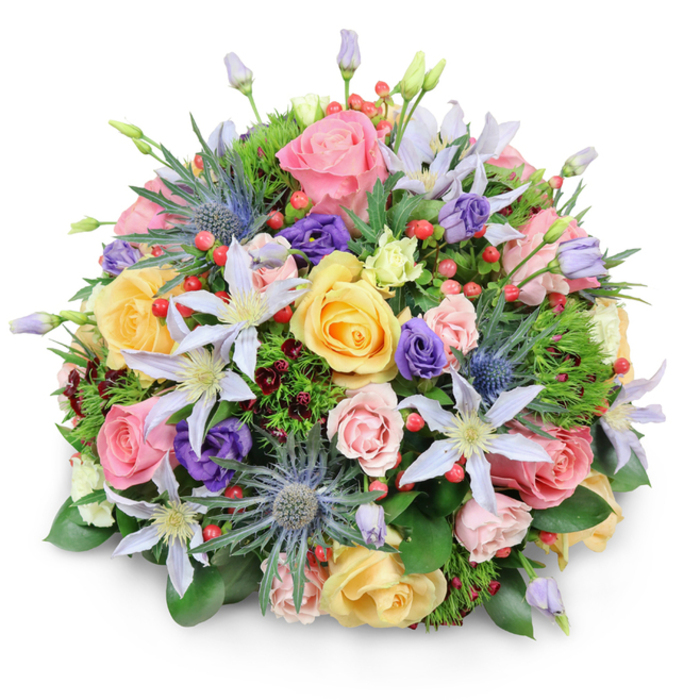 Presented on a pristine white background and photographed with soft, directional light, this densely packed, domed bouquet demonstrates considered floral architecture and a harmonious blend of colours and textures. The composition is anchored by numerous garden roses in gentle pinks, creamy peaches and warm buttery yellows, each bloom at a slightly different stage of opening so the eye travels across layers of unfurling petals. Interspersed are delicate clematis blossoms in shades from white to pale lavender, their star-shaped forms and pale centres offering moments of light within the mass of roses. Several blue eryngium or sea holly thistles introduce striking, spiky metallic-blue heads that give the arrangement an almost sculptural silhouette, while purple lisianthus in various forms - closed buds and open cups - add soft, velvety depth. Bright red hypericum berries appear in small clusters, providing vivid punctuation and a glossy texture against the matte petals. A bed of varied foliage - broad glossy leaves, finer feathery greens and hints of deep burgundy filler foliage - nests the blooms and creates a lush, verdant framework. The bouquet casts a soft shadow on the white surface, emphasizing its rounded volume as if ready for delivery to a riverside flat near the Embankment or as a focal point at a dinner in rooms looking toward St Martin-in-the-Fields. Crafted with an eye for tactile contrast, delicate scent layering and seasonally fresh stems, this arrangement from Flower Delivery Charing Cross reads as both joyful and composed - fitting for celebrations, warm thank-you gestures or quiet, dignified sympathy.