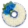A bespoke funeral tribute expertly shaped into the numeral '0', shown from above against a clean white background. The form is completely covered in a dense cushion of small white spray chrysanthemum florets whose tightly packed heads create a soft, cloud-like texture that reads as both comforting and quietly luminous. A narrow, deep royal blue border-crafted from pleated satin ribbon and echoing the colour of possibly dyed blooms-traces the outer and inner edges of the zero, giving the piece a refined scalloped frame that emphasizes the character of the number. Nestled on the upper left curve is a careful cluster of three vivid royal blue roses; their petals unfurl with a velvety sheen and are set against a few glossy dark green leaves that add natural depth and a subtle, living contrast. The lighting is soft and even, skimming over petals and ruffles so shadows fall gently into the hollows of the numeral, lending the piece a solemn dignity without harshness. As a florist working in Charing Cross I imagine this as a personalised element in a larger memorial display-perhaps paired with adjoining numbers for an age or a meaningful date-and it sits comfortably beside tributes delivered to local chapels near the Strand or quiet services around the Embankment. The combination of pristine white chrysanthemums and tranquil blue roses speaks of respect, peace, and steadfast remembrance; the satin pleating brings a formal finish appropriate for a wake or funeral service. This arrangement reads as a carefully considered vessel for memory, made to express sympathy and honour with measured elegance and local craftsmanship.
