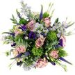 In this overhead image, the bouquet forms a generous, rounded cluster of blooms and foliage, almost like a miniature garden gathered onto a pristine white tabletop in a Charing Cross townhouse. The dominant flowers are large roses in shades of dusty pink, blush, and soft mauve, their petals opening wide in graceful spirals that reveal velvety inner layers and slightly green-tinged outer edges, a sure sign of their freshness. Floating among these sumptuous roses are small, aster-like blossoms in tones of lavender and cool purple, their neat yellow centres dotting the composition like tiny drops of sunshine and bringing a sense of lightness and cheer. Rich purple and deep indigo lisianthus blooms add pockets of intensity, their ruffled, bell-shaped forms introducing both depth and a touch of drama that feels perfectly suited to the nearby West End theatres. Rising delicately through this mix are slender stalks of purple veronica, composed of countless tiny florets, which lend graceful height and a feeling of gentle motion, as if caught by a soft breeze off the Thames. Nestled throughout, bright chartreuse green spheres reminiscent of Green Trick dianthus provide playful contrast, their tufted, moss-like texture standing out against the smoother petals and creating a modern, sculptural effect. Silvery eucalyptus leaves curl around the edges and weave between the flowers, along with other green foliage and several tight buds that promise future blooms, adding depth and a calm, cool undertone to the palette. Crafted with the practiced eye of Flower Delivery Charing Cross, this bouquet feels both joyful and sophisticated, ideal for marking milestones, sending warm wishes to an office near the Strand, or brightening a quiet evening at home in central London.